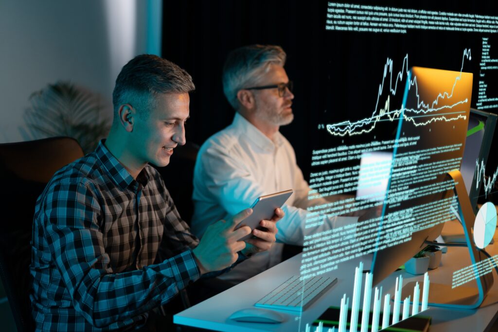Two,Businessmen,Analyzing,Data,On,Digital,Screens,In,Modern,Office.